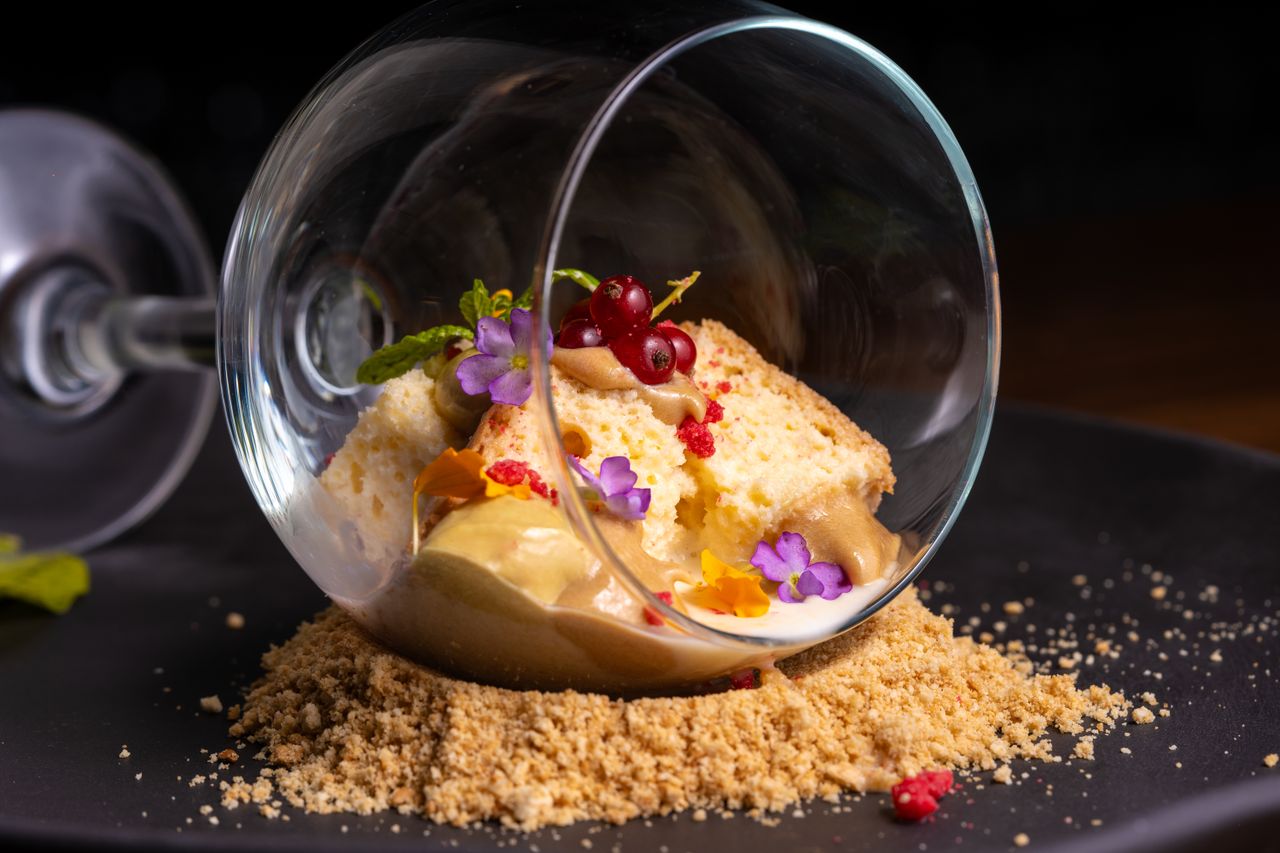Innovative dessert served in an upside-down glass with colorful garnishes on a dark plate.